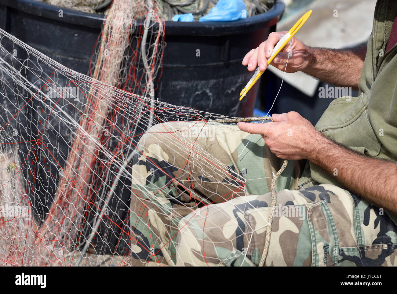 Hände bei der Arbeit am Fischernetz mit einem Werkzeug Stockfoto