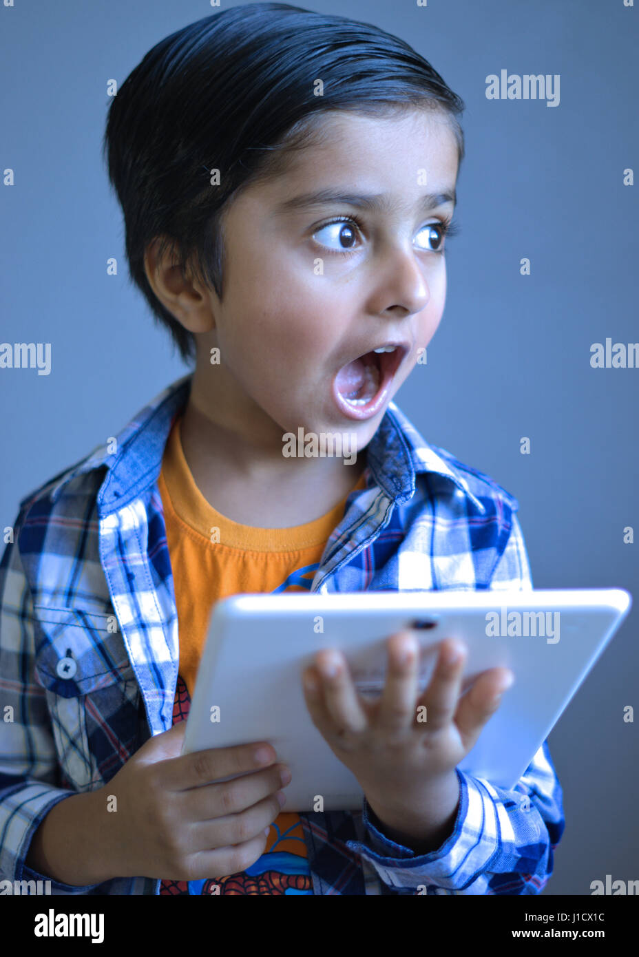 Kind mit überraschten Blick hält einen Tablet-Computer, wegschauen von der Kameralinse. Stockfoto