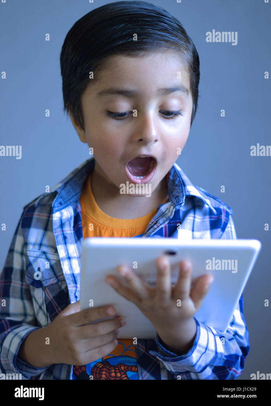 Kind mit überraschten Blick hält einen Tabletcomputer Stockfoto