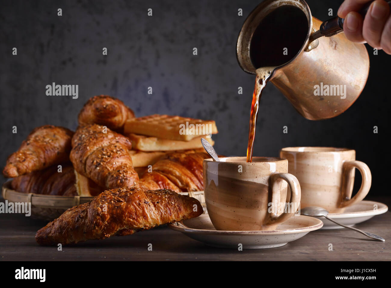 Alte Kupfer Kaffeemaschine. Frischer heißer Kaffee in die Tasse gegossen. Frühstück mit Croissants, schwarzen Kaffee und frisch gebackenen Waffeln. Stockfoto