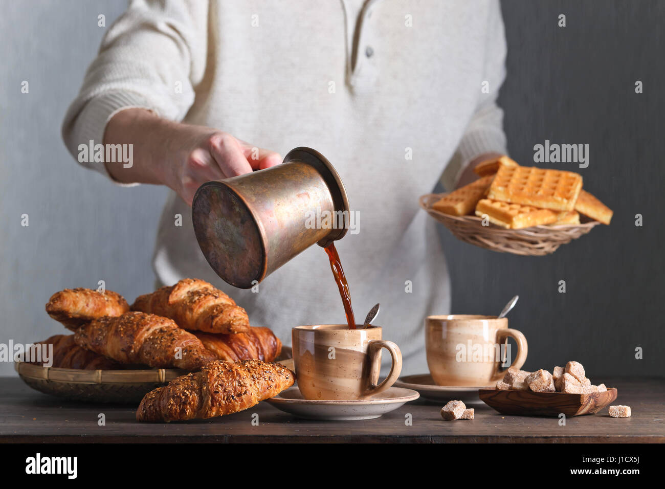 Frühstück mit Croissants, schwarzen Kaffee und frisch gebackenen Waffeln. Alte Kupfer Kaffeemaschine. Frischer heißer Kaffee in die Tasse gegossen. Stockfoto