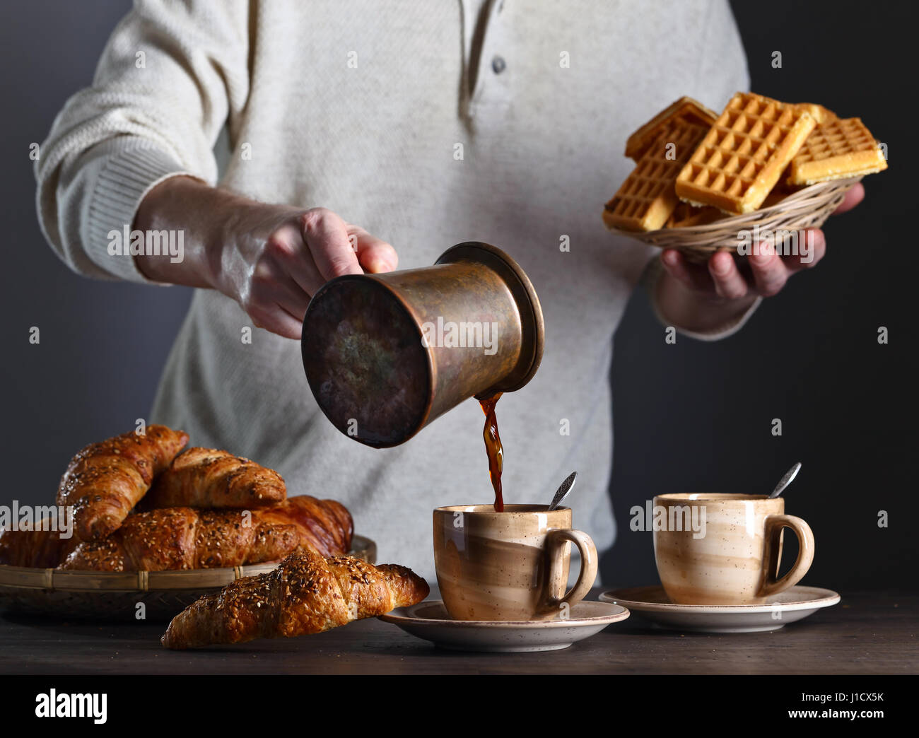 Frühstück mit Croissants, schwarzen Kaffee und frisch gebackenen Waffeln. Alte Kupfer Kaffeemaschine. Frischer heißer Kaffee in die Tasse gegossen. Stockfoto