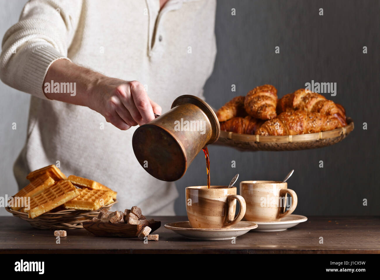 Frühstück mit Croissants, schwarzen Kaffee und frisch gebackenen Waffeln. Alte Kupfer Kaffeemaschine. Frischer heißer Kaffee in die Tasse gegossen. Stockfoto