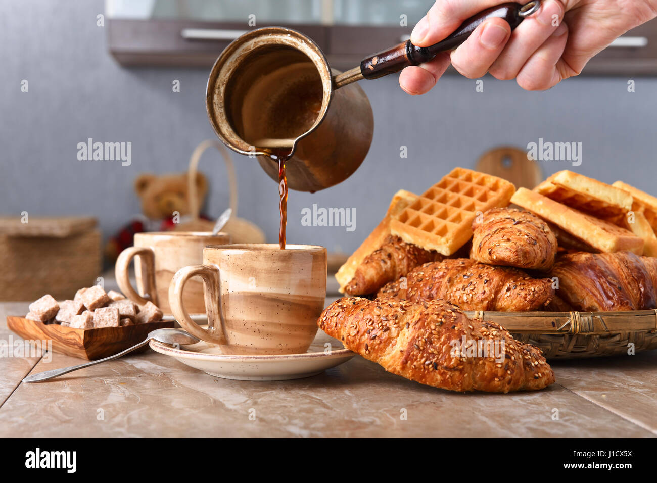 Alte Kupfer Kaffeemaschine. Frischer heißer Kaffee in die Tasse gegossen. Frühstück mit Croissants, schwarzen Kaffee und frisch gebackenen Waffeln. Stockfoto