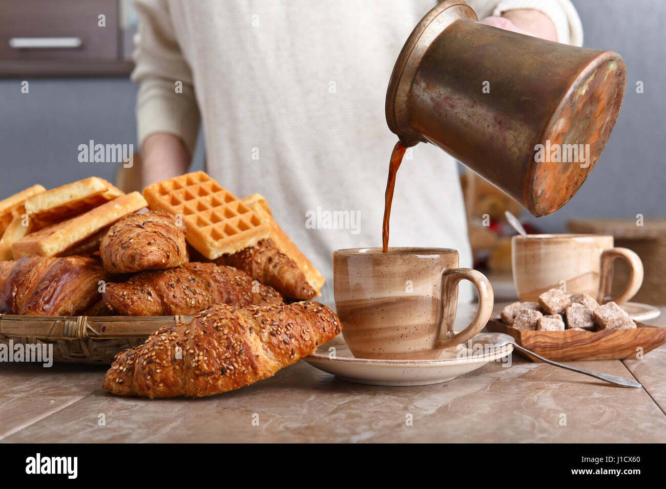 Frühstück mit Croissants, schwarzen Kaffee und frisch gebackenen Waffeln. Alte Kupfer Kaffeemaschine. Frischer heißer Kaffee in die Tasse gegossen. Stockfoto