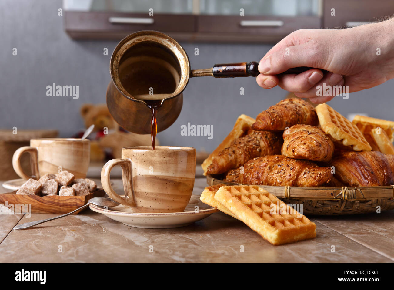 Alte Kupfer Kaffeemaschine. Frischer heißer Kaffee in die Tasse gegossen. Frühstück mit Croissants, schwarzen Kaffee und frisch gebackenen Waffeln. Stockfoto