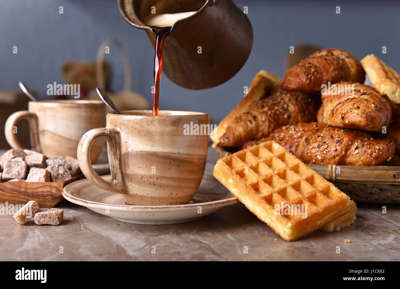 Alte Kupfer Kaffeemaschine. Frischer heißer Kaffee in die Tasse gegossen. Frühstück mit Croissants, schwarzen Kaffee und frisch gebackenen Waffeln. Stockfoto