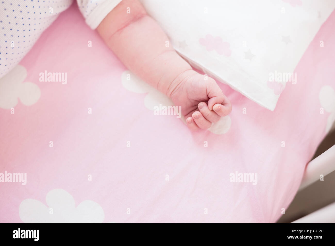 Detail-Aufnahme von Babys Hand in pink Sheets mit Wolkenmuster. Geringe Schärfentiefe Feld, natürliches Licht. Stockfoto