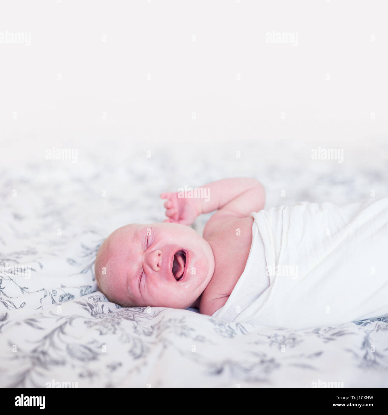 Neugeborenes Baby im Bett Weinen. Natürliches Licht, geringe Schärfentiefe, Textfreiraum. Stockfoto