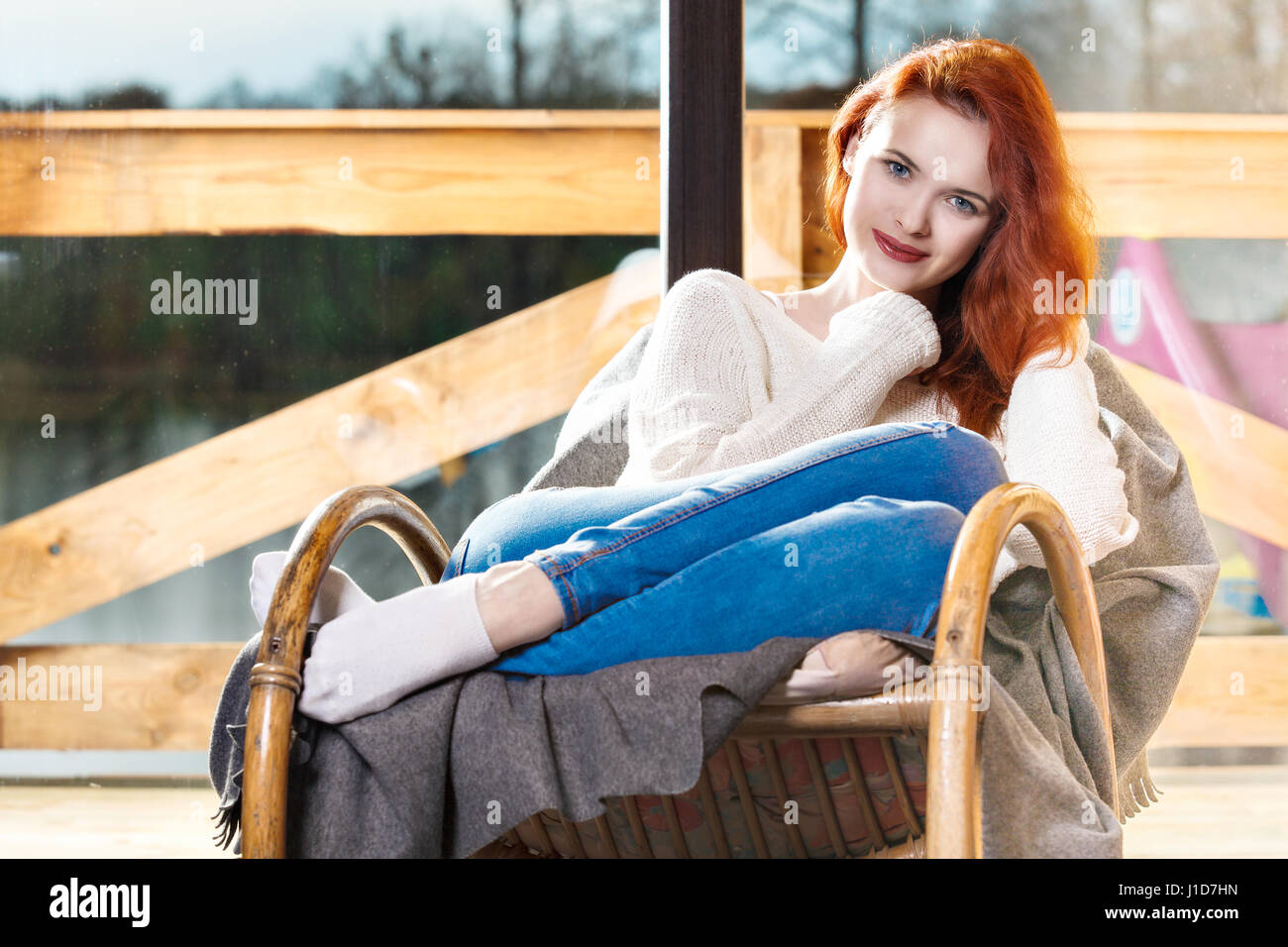 Attraktive rothaarige Frau ruht auf Schaukelstuhl vor Fenster sitzen. Ruhe und Gemütlichkeit. Stockfoto