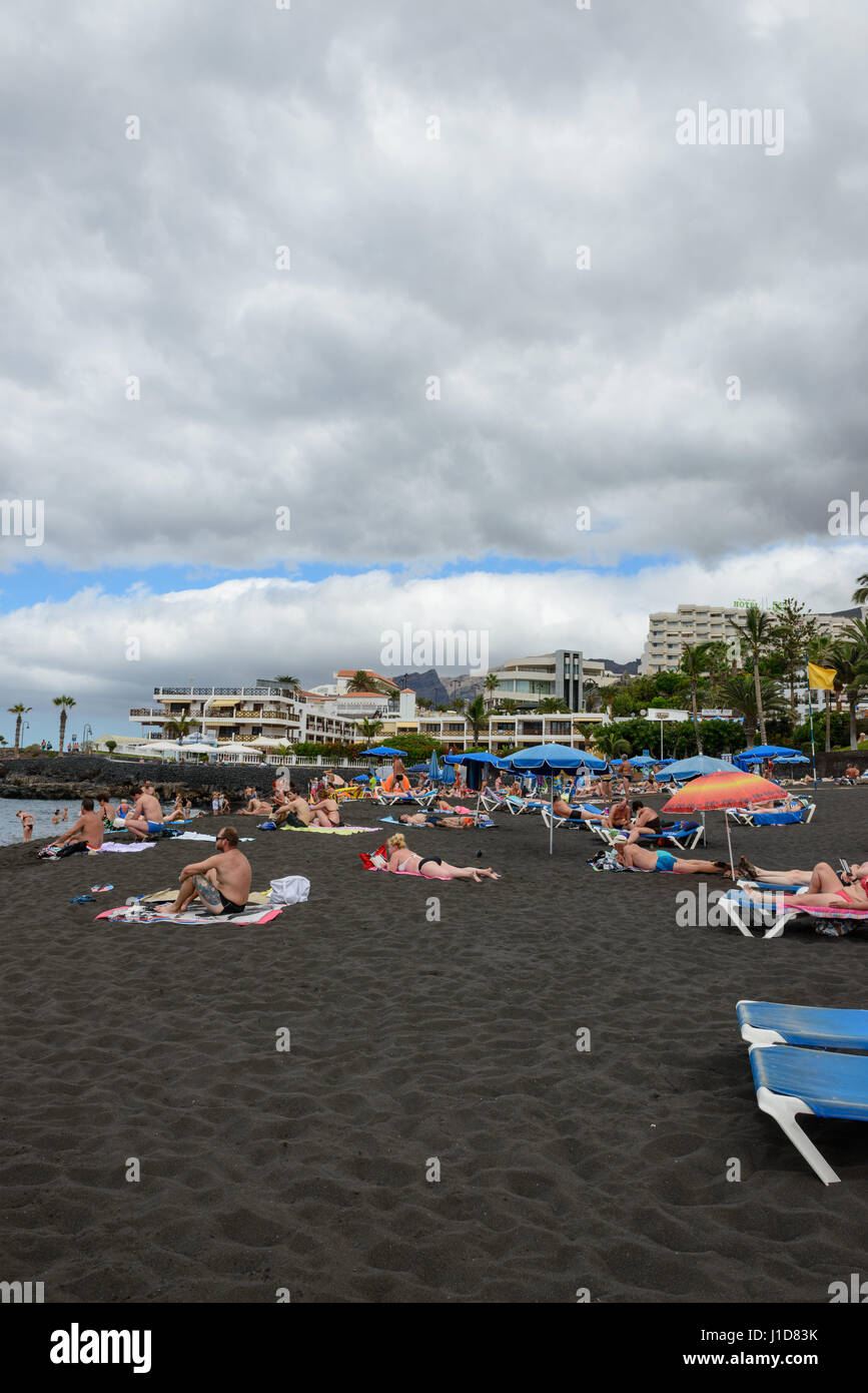 Arena-Strand mit Touristen auf den schwarzen vulkanischen Sand im bewölkten Tag in Puerto de Santiago, Teneriffa, Kanarische Inseln, Spanien. Stockfoto