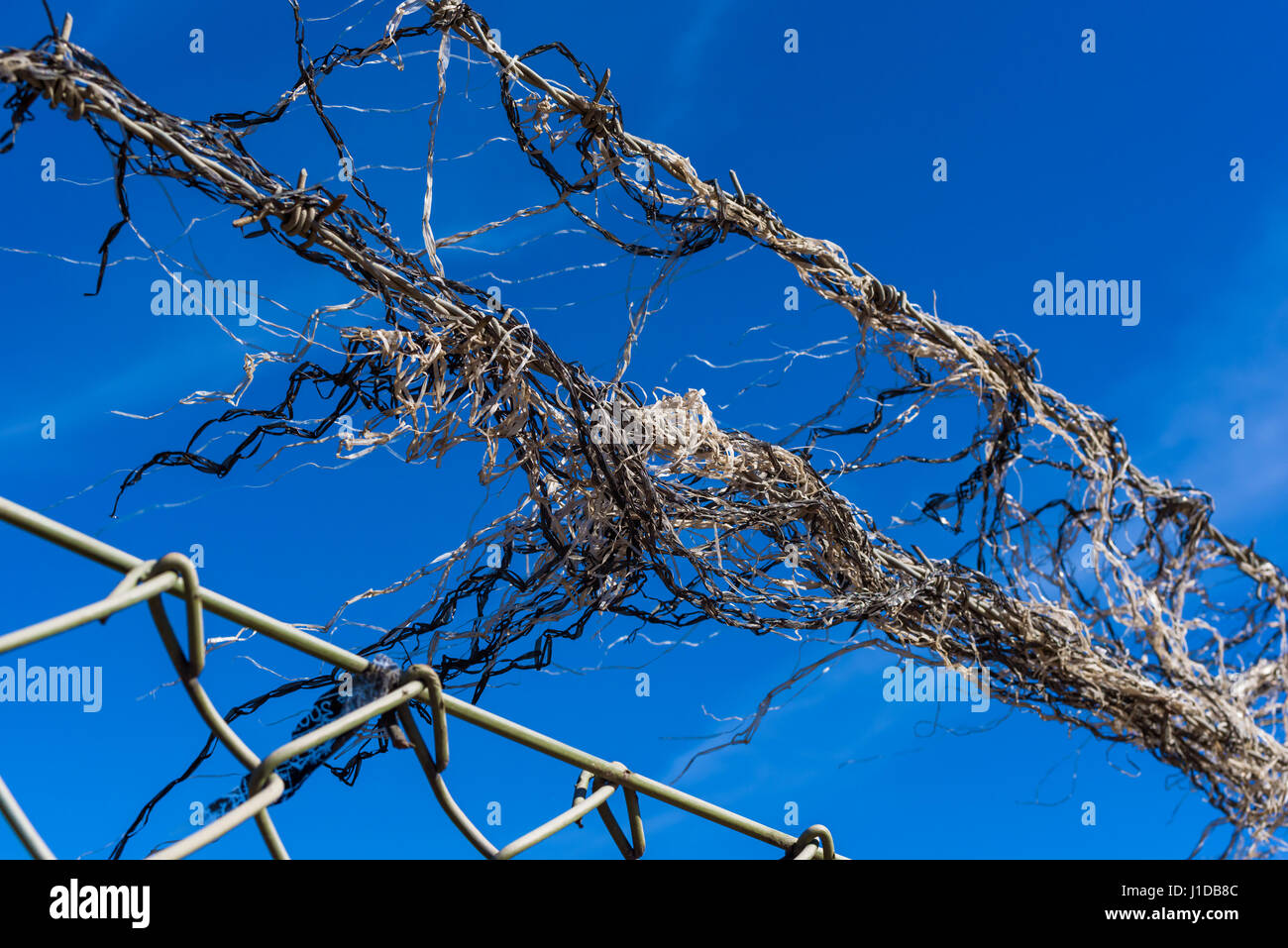 Kunststoff Schutt im Wind wehen, da es auf einigen Stacheldraht über einen saldierten Zaun stecken. Blauen Himmel im Hintergrund. Stockfoto