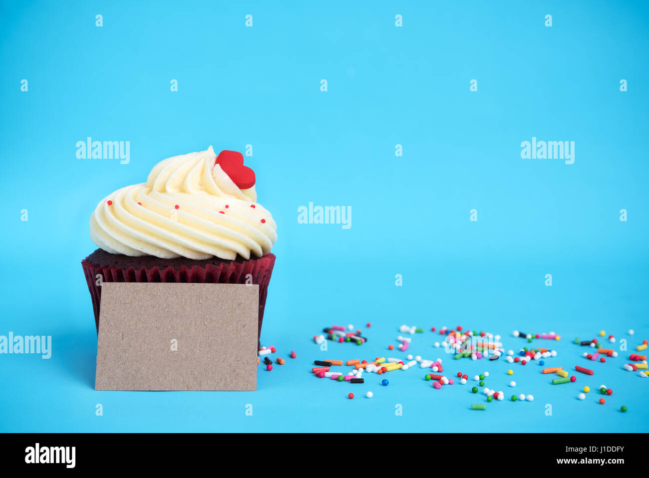Cupcake mit roten Herzen, bunten Streuseln und braun Hinweis auf blauem Hintergrund mit Textfreiraum Stockfoto