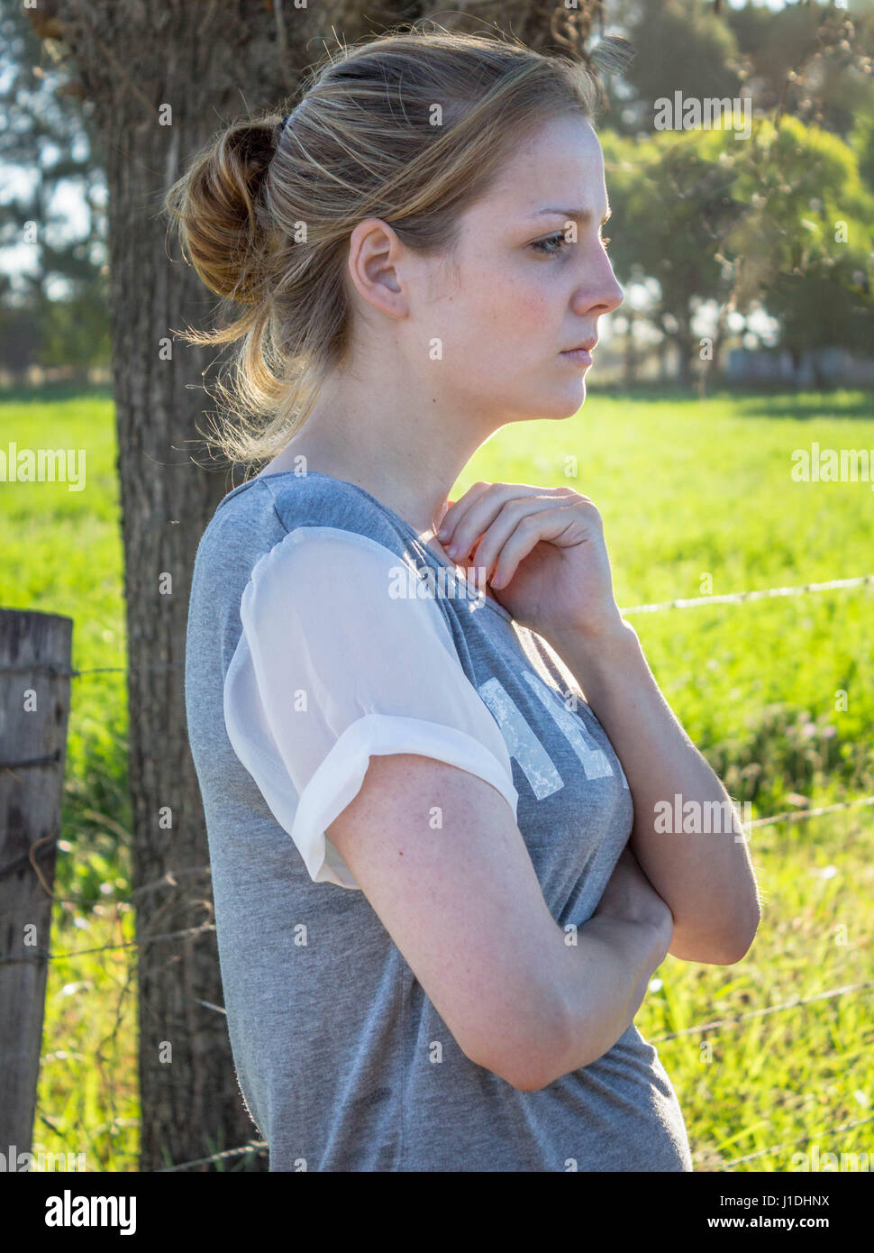 Porträt von schweren jungen blonden Frau, die auf der Suche voraus und Weg von der Kamera stehend im Schatten unter einem Baum in einer ländlichen einstellen - vertikale Foto Stockfoto