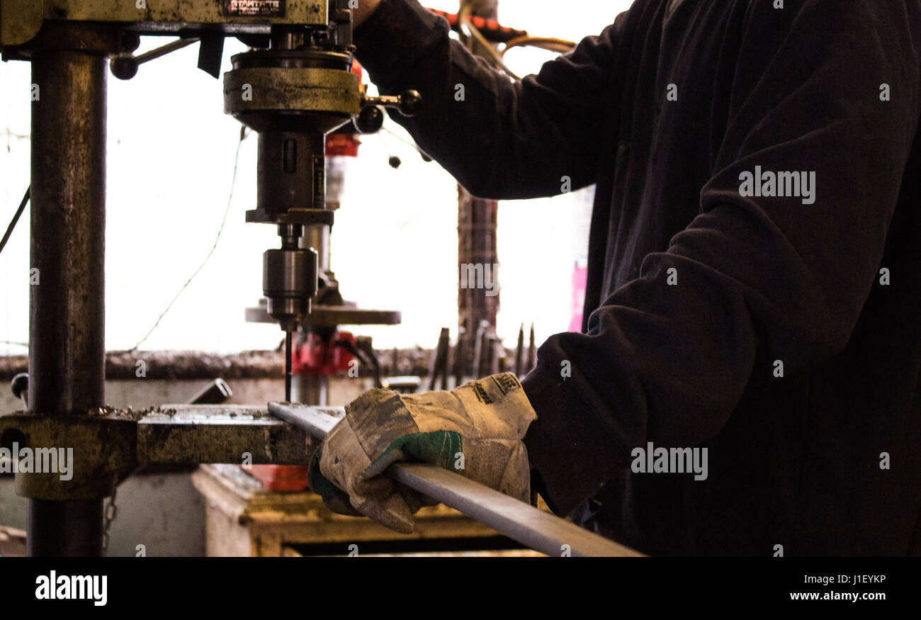 Bau Arbeiter Bohrer Loch im Metall eiserner mit industriellen Bohrer in einem dunklen Workshop / Spezialwerkzeug / Fabrik Stockfoto