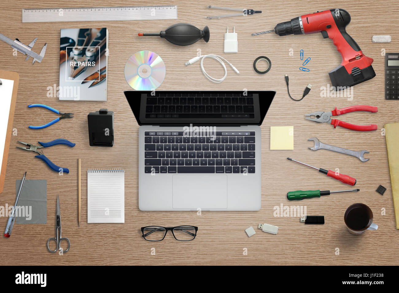 Computer-Reparatur-Schreibtisch. Laptop mit Werkzeugen umgeben. Schraube, Schraubenzieher, Scheren, Zangen, Bohrer, Schlüssel, Reinigungswerkzeug, Buch neben. Stockfoto