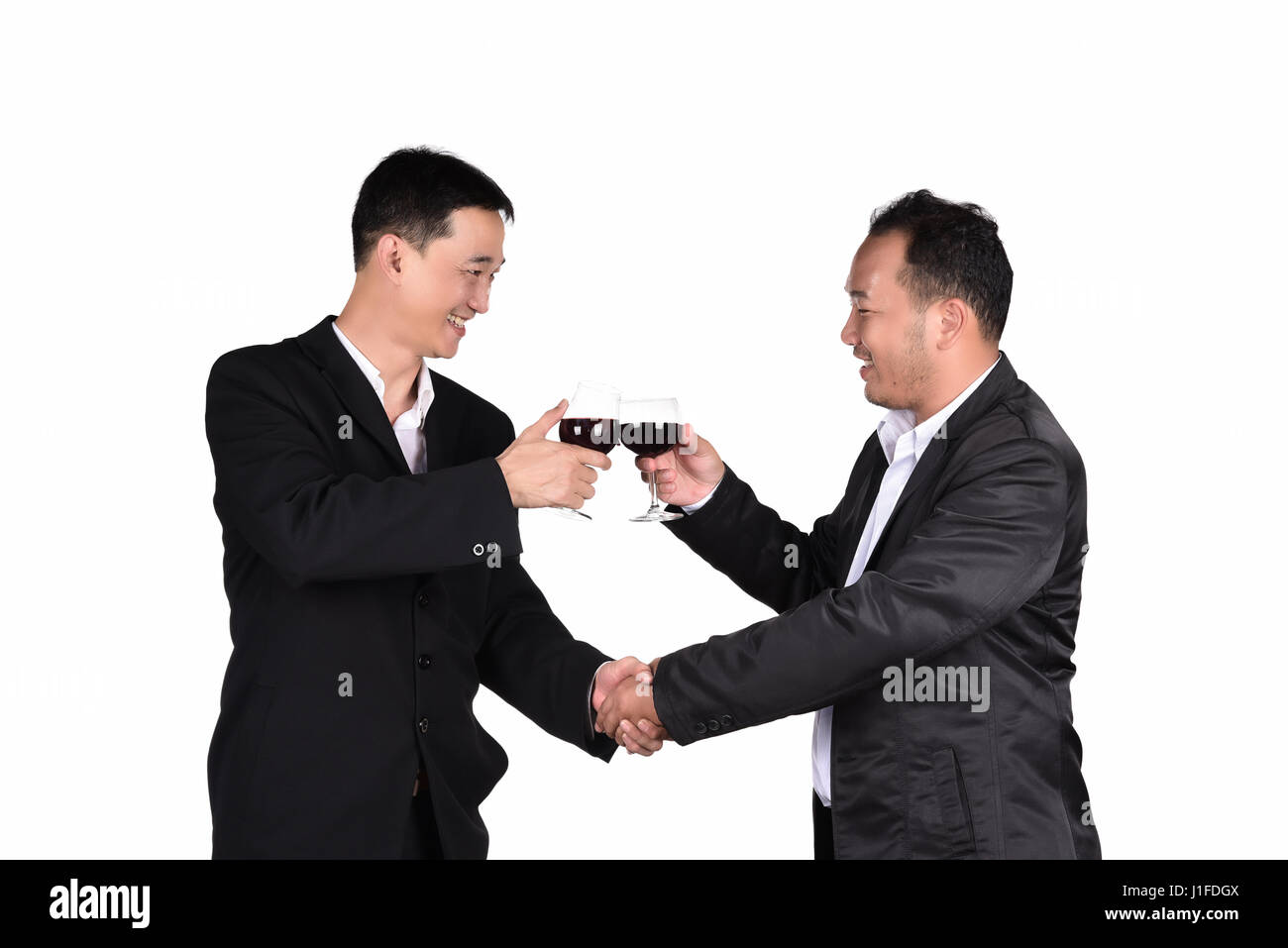 Zwei junge Unternehmer Handshake in Anzügen sind lächelnd und klingende Gläser alkoholisches Getränk zusammen isoliert auf weißem Hintergrund Stockfoto