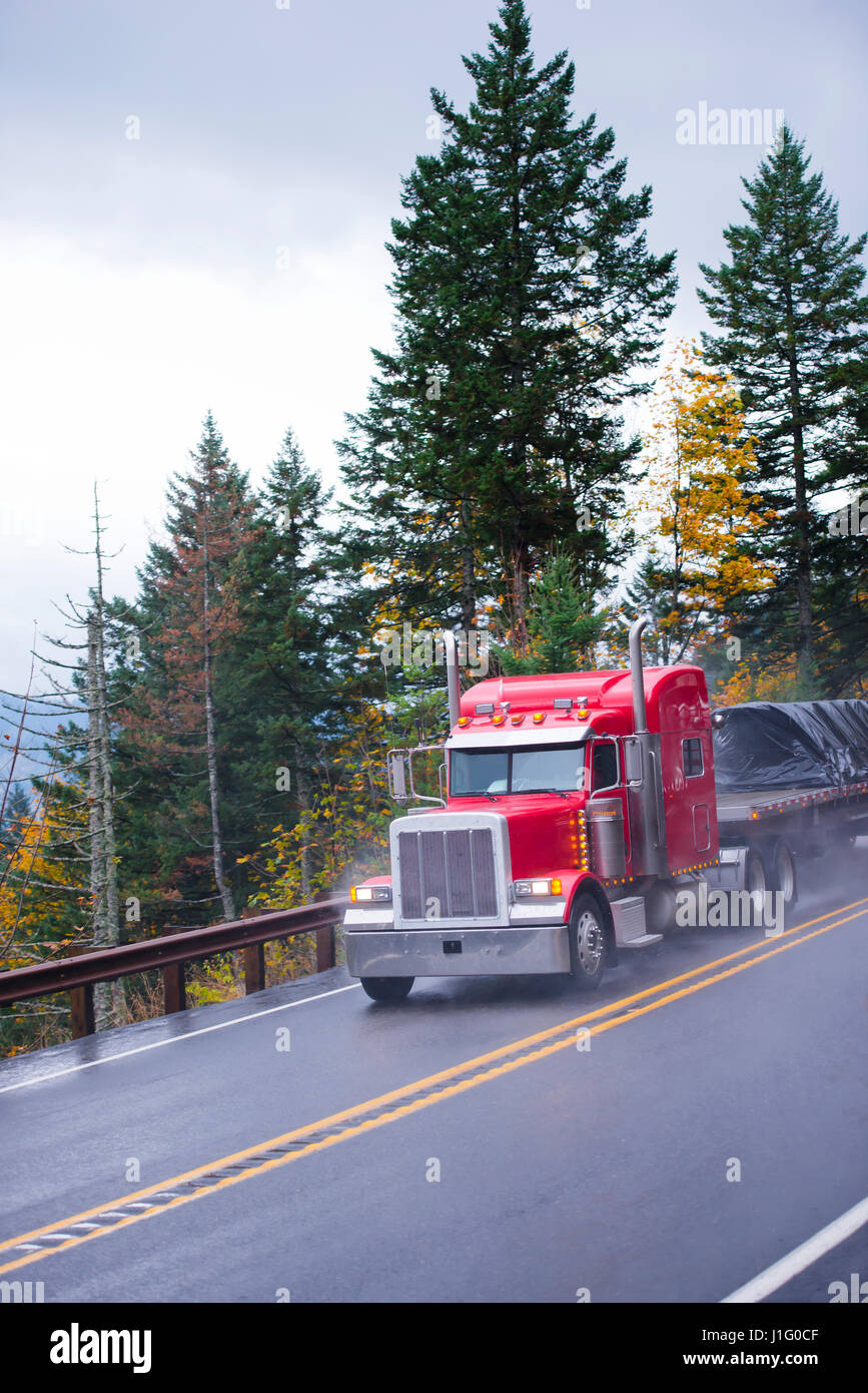 Große rote Semi Truck klassischen amerikanischen Stil mit traditionellen Endrohren und andere Chrom-Akzenten und Tieflader auf die sind beförderten Güter Stockfoto Große rote Semi Truck klassischen amerikanischen Stil mit traditionellen Endrohren und andere Chrom-Akzenten und Tieflader auf die sind beförderten Güter Stockfoto