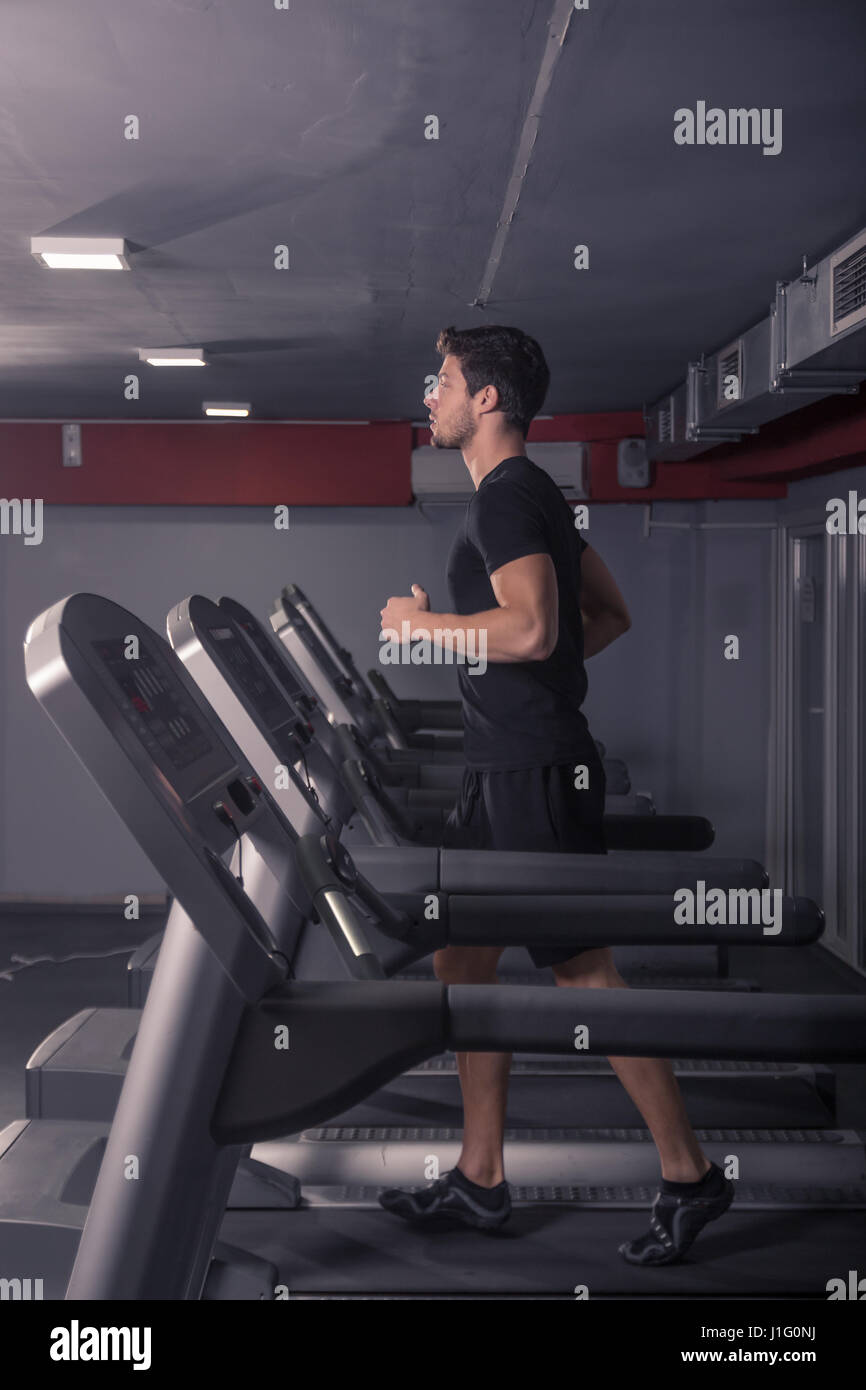 sportliche Passform schlanke junge Mann läuft auf Laufband. Viele Laufbänder, Linie, im Innenbereich mehrere, Fitness-Studio. Stockfoto