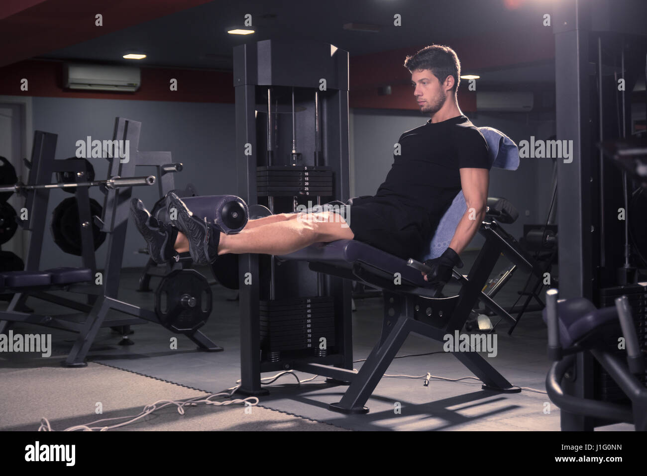 jung, fit schlank sportlicher Mann, Beinstrecker, drinnen sitzen Fitness-Studio, Fitness-Geräte. Stockfoto