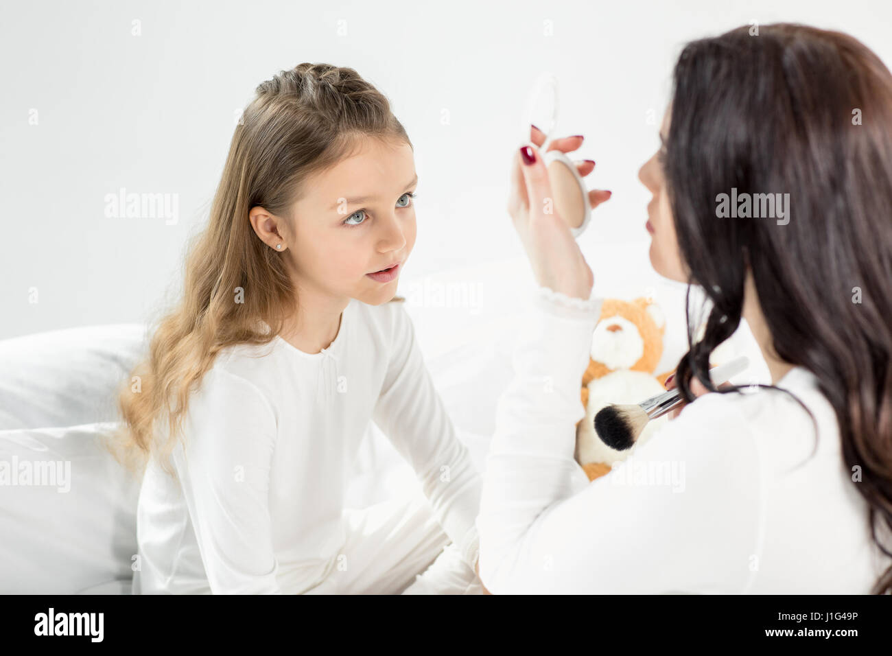 Niedliche kleine Mädchen im Schlafanzug sah Mutter mit Kosmetikspiegel Stockfoto