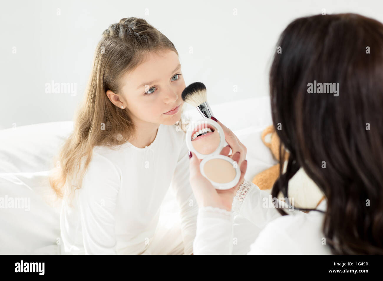 Mutter mit Kosmetikspiegel und Pinsel beim Schminken Töchterchen Stockfoto