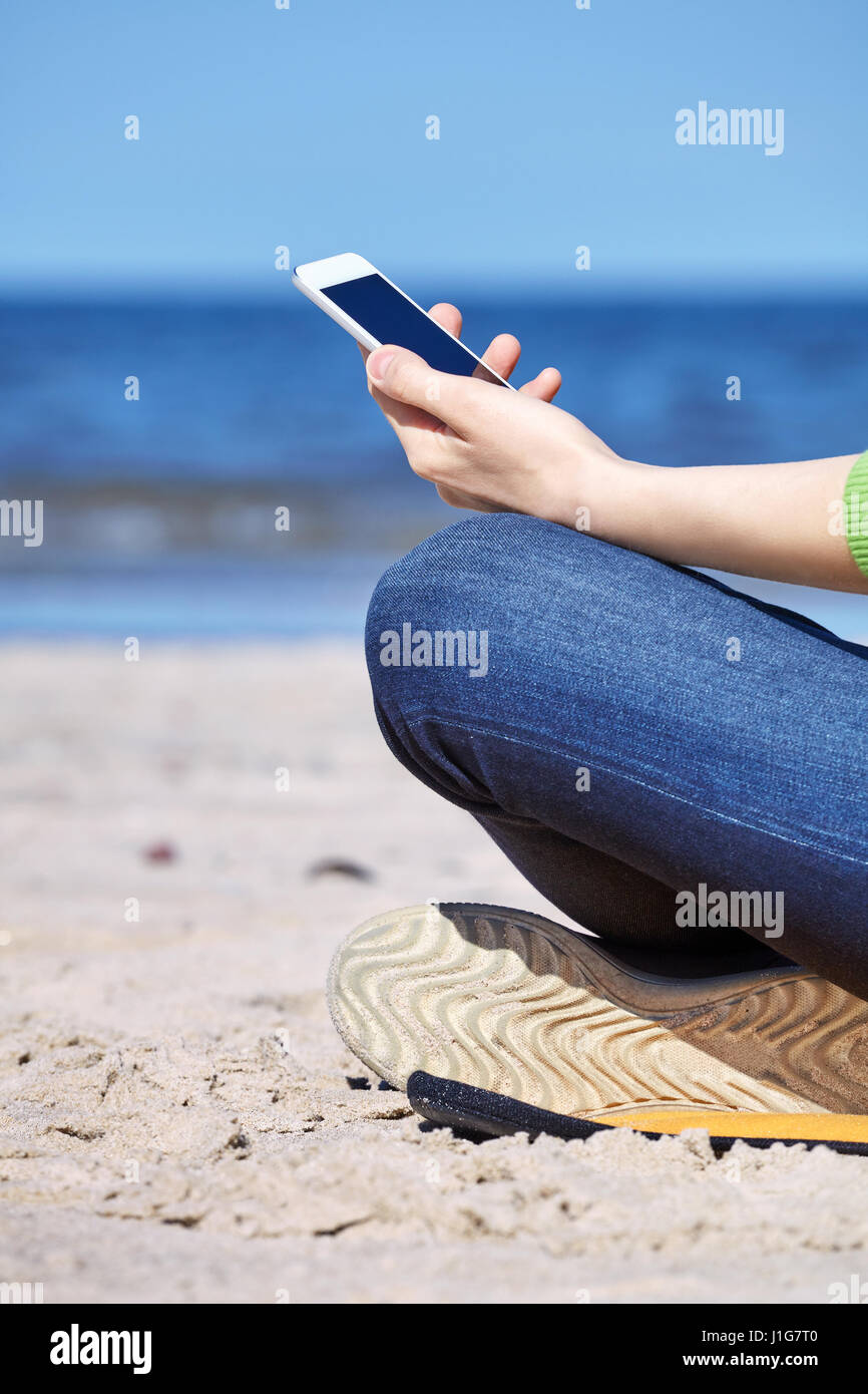 Nahaufnahme einer Frau mit Smartphone an einem Strand, Seitenansicht. Stockfoto