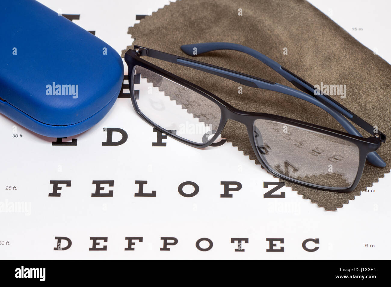 Schwarze Brillen, braun Mikrofaser Tuch und blau Schutzhülle mit weißem Auge Diagramm Nahaufnahme Reinigung lesen Stockfoto