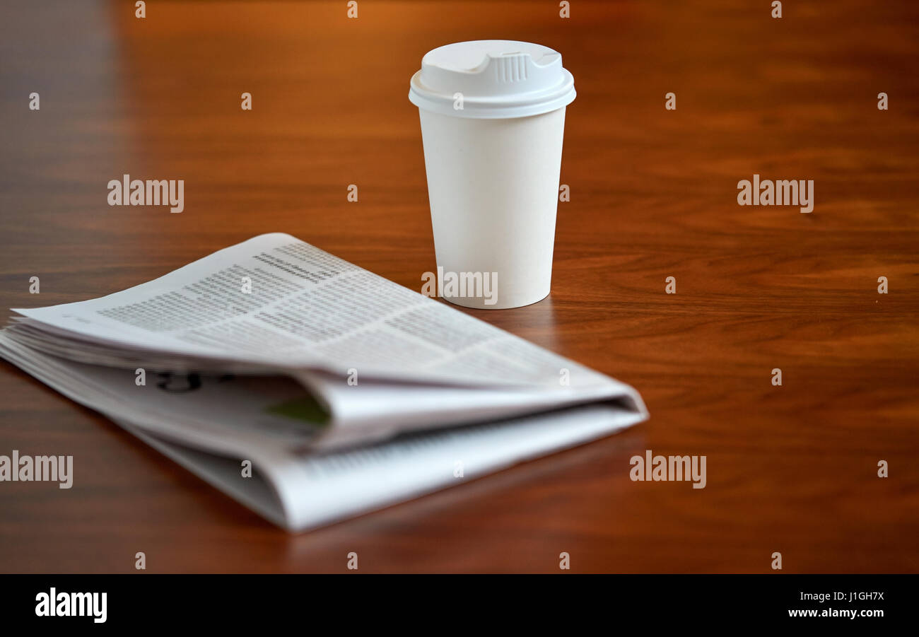 Kaffee trinken in Pappbecher und Zeitung auf Tisch Stockfoto