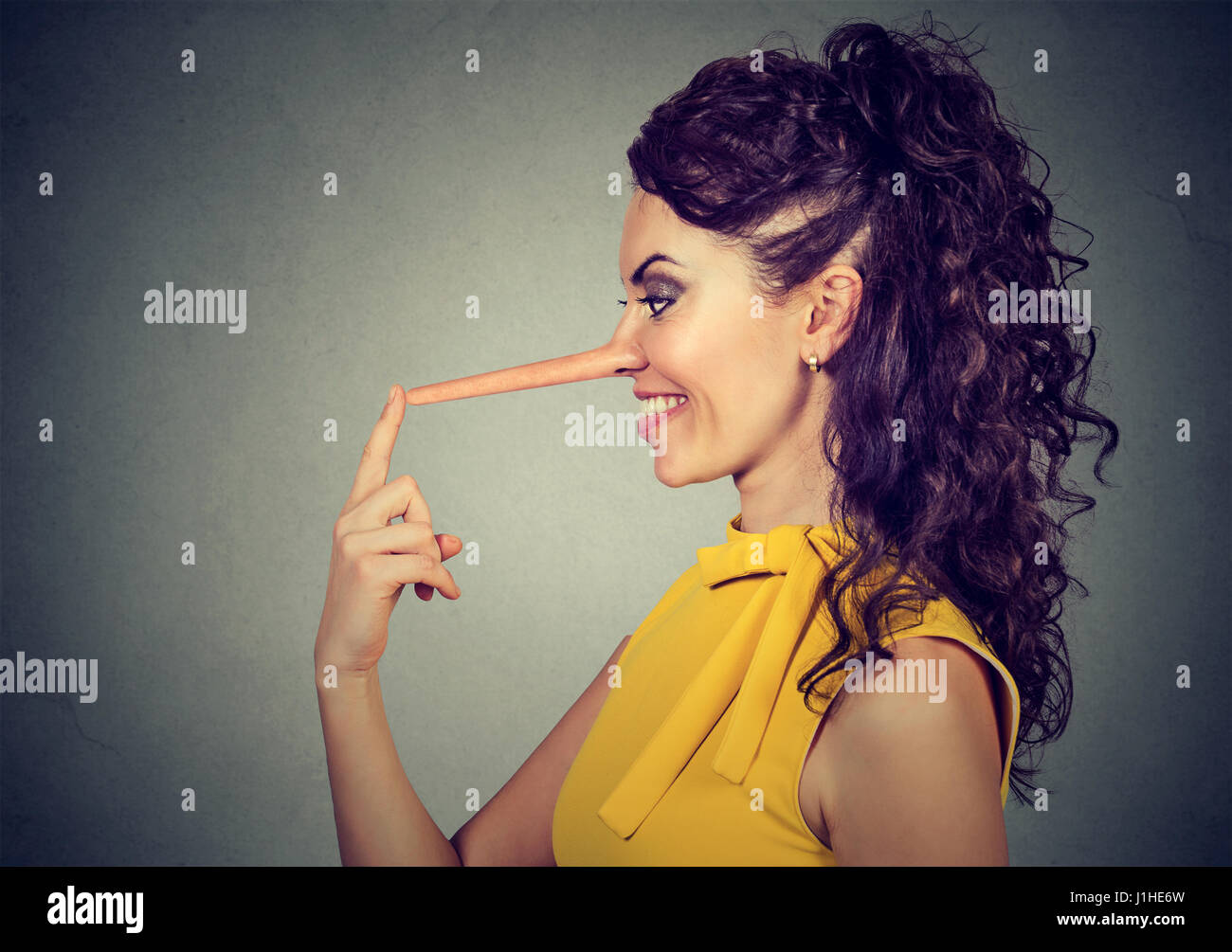 Seitenansicht einer lächelnden Frau mit langer Nase auf graue Wand Hintergrund isoliert. Lügner-Konzept. Menschlichen Gesichtsausdruck, Emotionen, Gefühle Stockfoto