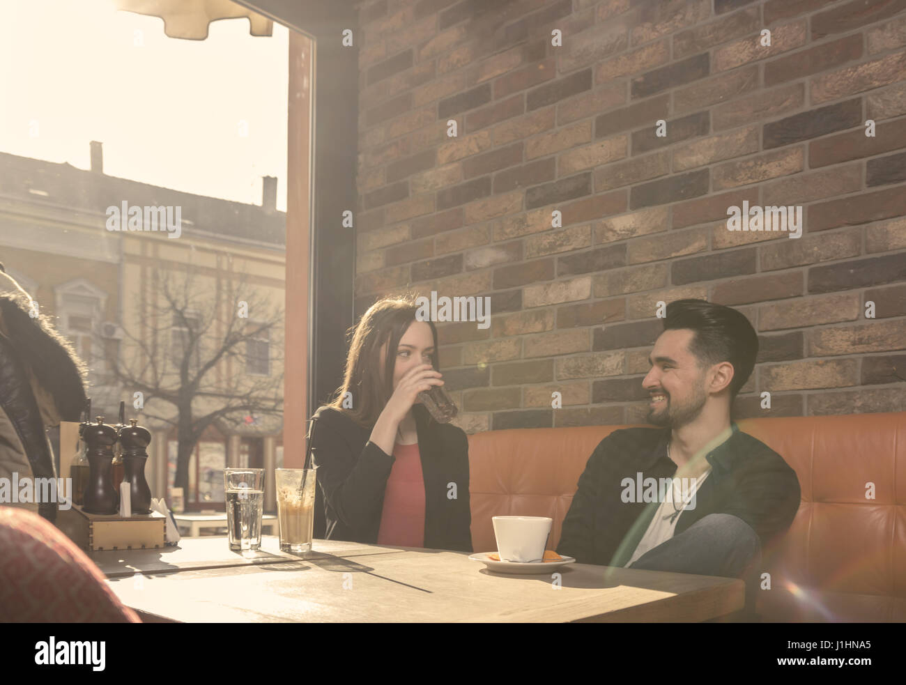 20er Jahre, junger Erwachsener Mann Frau lächelnd sprechende Lebensstil sitzen Caffe drinnen, Trinkwasser Stockfoto