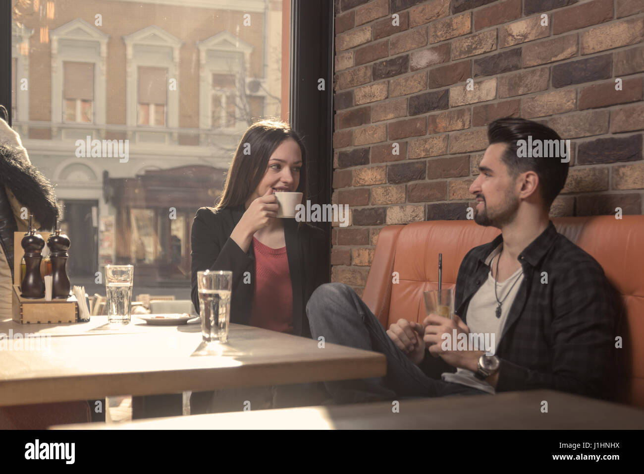 junge Erwachsene 20er Jahre Frau Mann Café trinken Cofe-Cup im Innenbereich, sonnigen Tag, Fenster sitzen Stockfoto