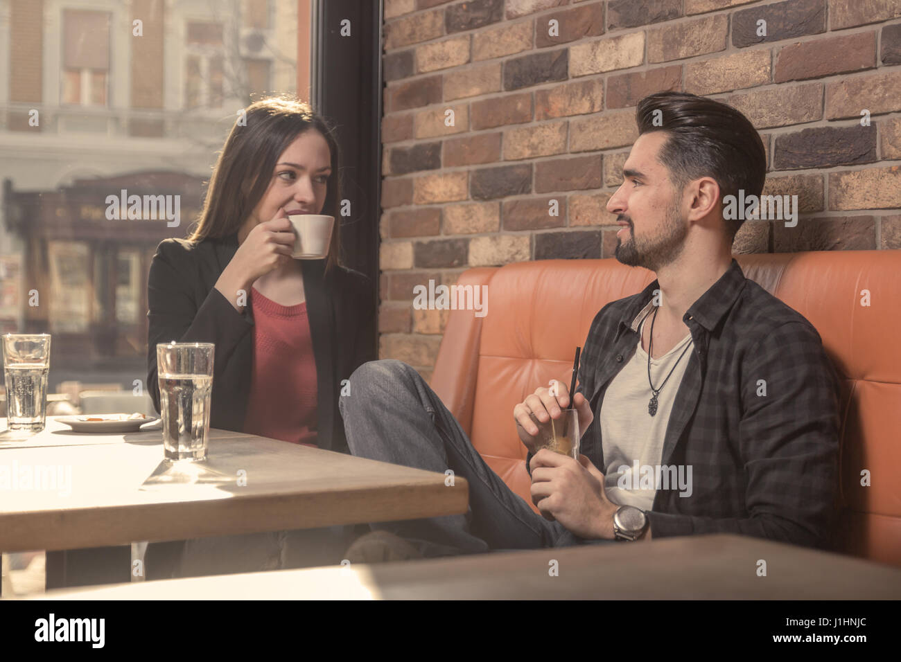 20er Jahre junger Erwachsener lächelnd sprechende Frau Mann Café trinken drinnen reden sitzen Tabelle Stockfoto