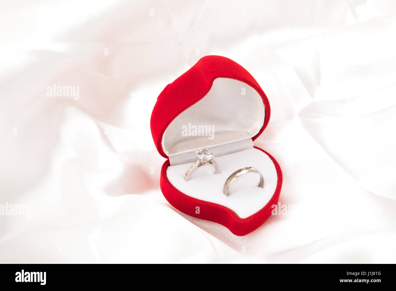 Ein sein und ihr Ehering in ein Herz geformt Ring Box - weiße satin Blatthintergrund. Stockfoto