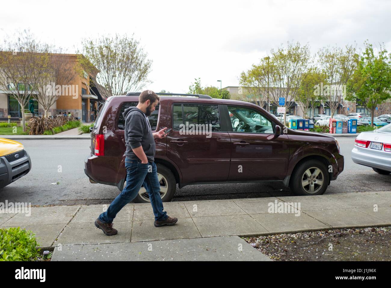 Ein junger Mann geht tausendjährigen Alter Technologie Arbeiter tragen einen Hoodie während der Überprüfung sein Handy in der Nähe der Googleplex Hauptquartier von Google Inc in das Silicon Valley Stadt Mountain View, Kalifornien, 7. April 2017. Stockfoto