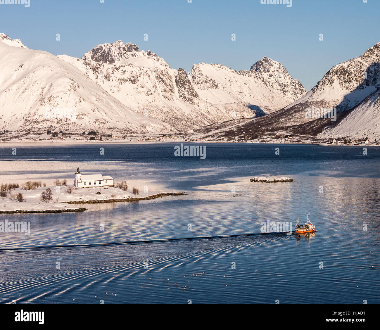 Sildpollnes Kirche mit einem vorbeifahrenden roten Fischerboot auf Austvagoya, Lofoten Inseln, Norwegen Stockfoto