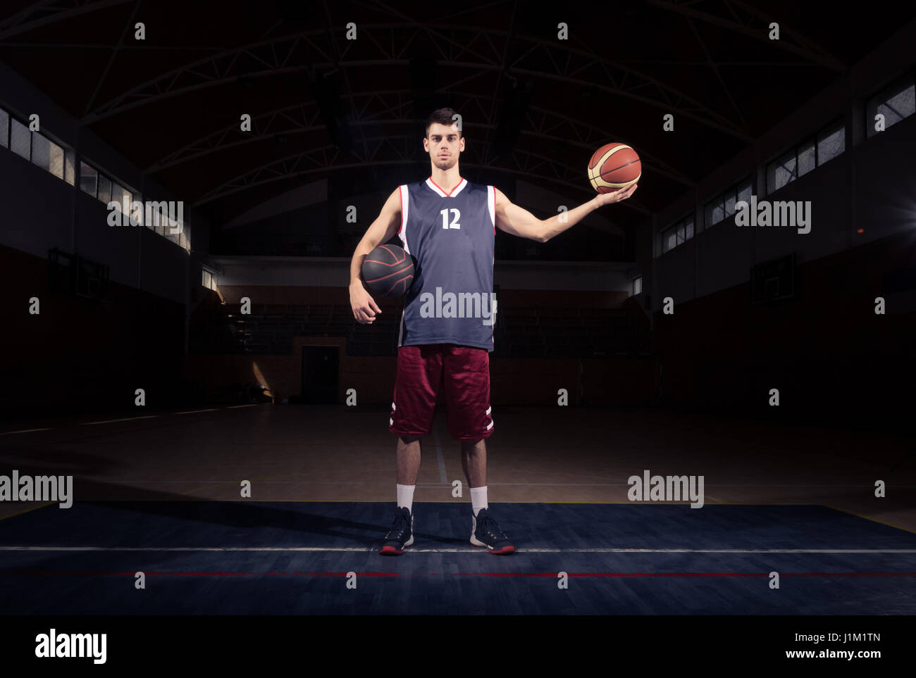 Basketball-Spieler halten zwei Kugeln, posieren, dunkle Basketballplatz im Innenbereich Stockfoto