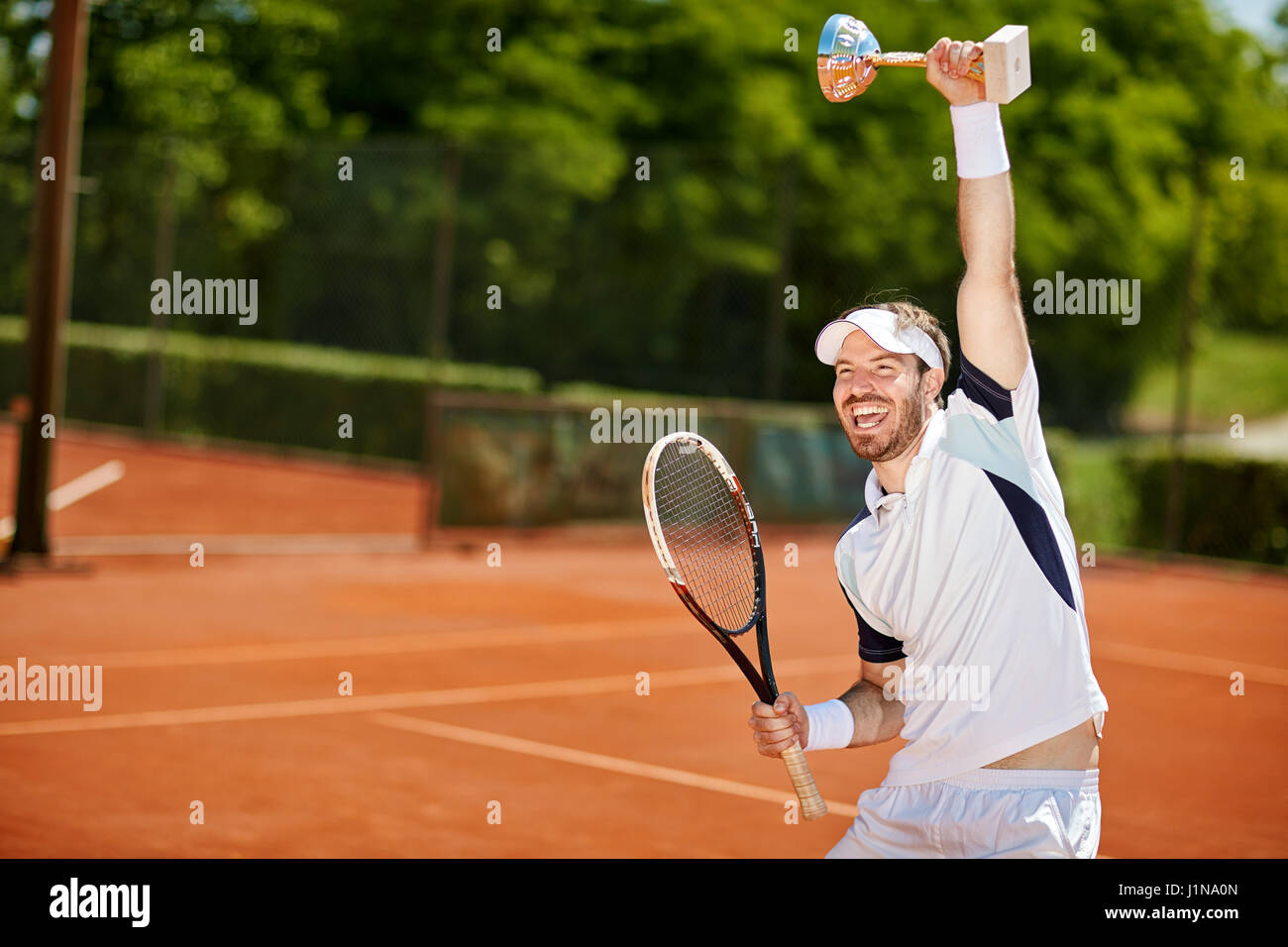 Glücklich Tennisspieler mit Kelch und Schläger nach Spiel Stockfoto