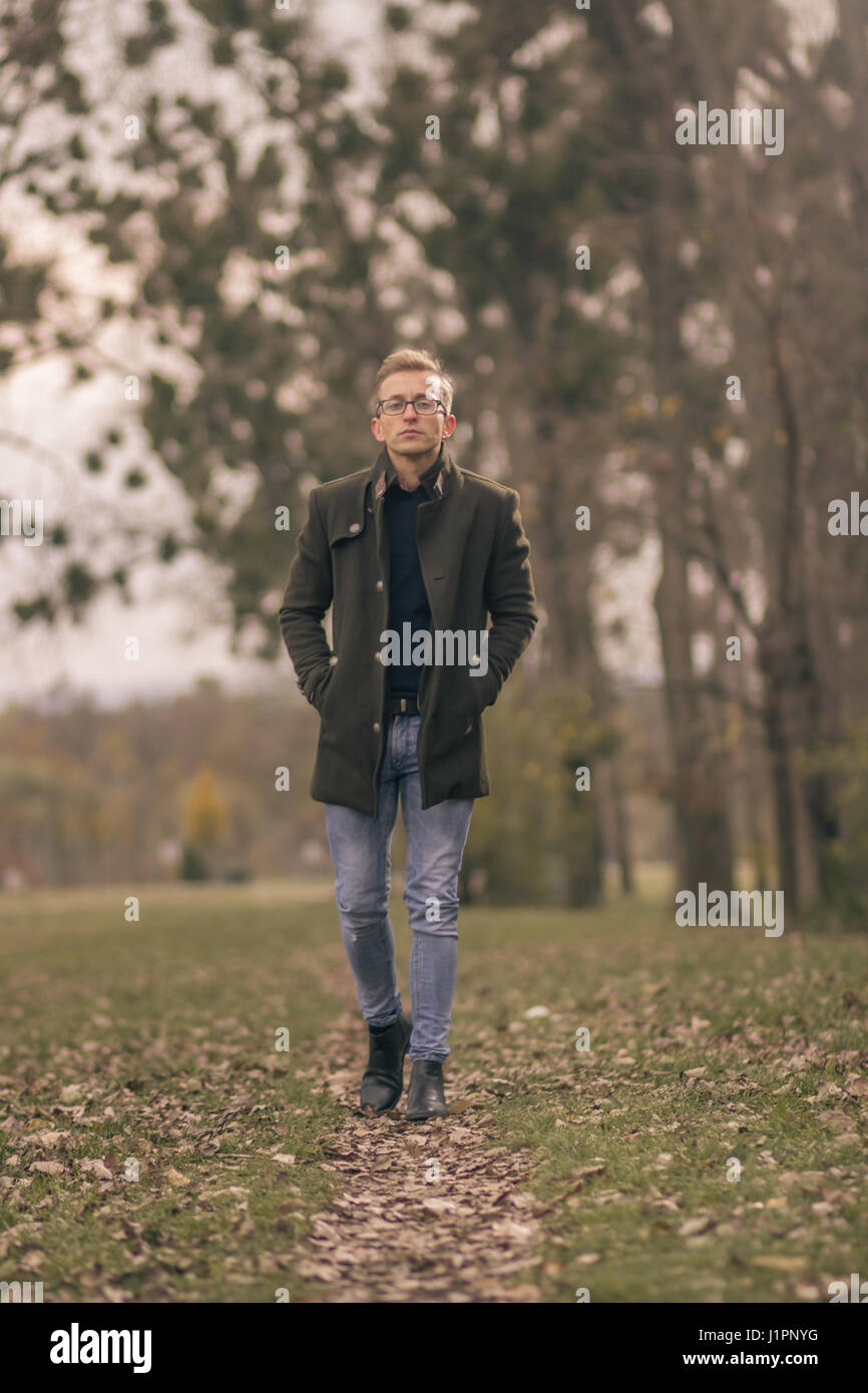 ein junger Mann, 20er Jahre, sieht gut aus, Lust auf Kleidung zu Fuß im Park allein. Kittel, Jeans, Stiefel. Herbst Blätter, Bäume, grüne Natur. Stockfoto