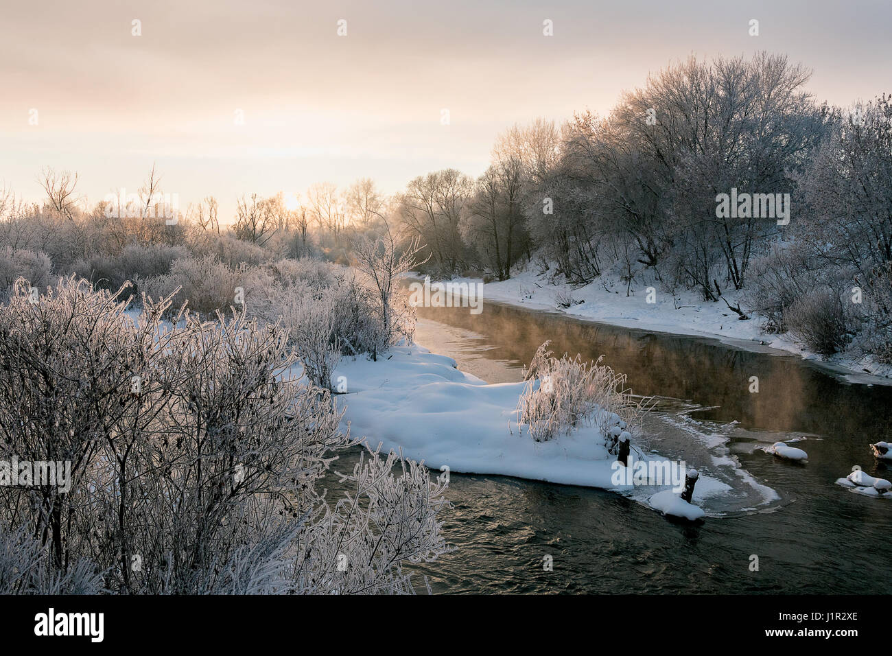fließt der Fluss im Winter unter den verschneiten Ufern Stockfoto