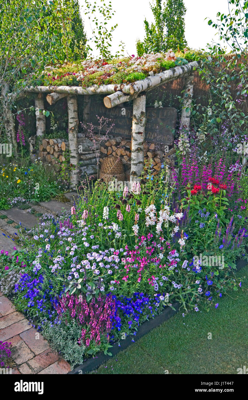 Eine bunt gemischte Blume Grenze mit Monarda "Cambridge Scarlet" und ein Sedum bedeckt Dach auf ein Gartenhäuschen Stockfoto