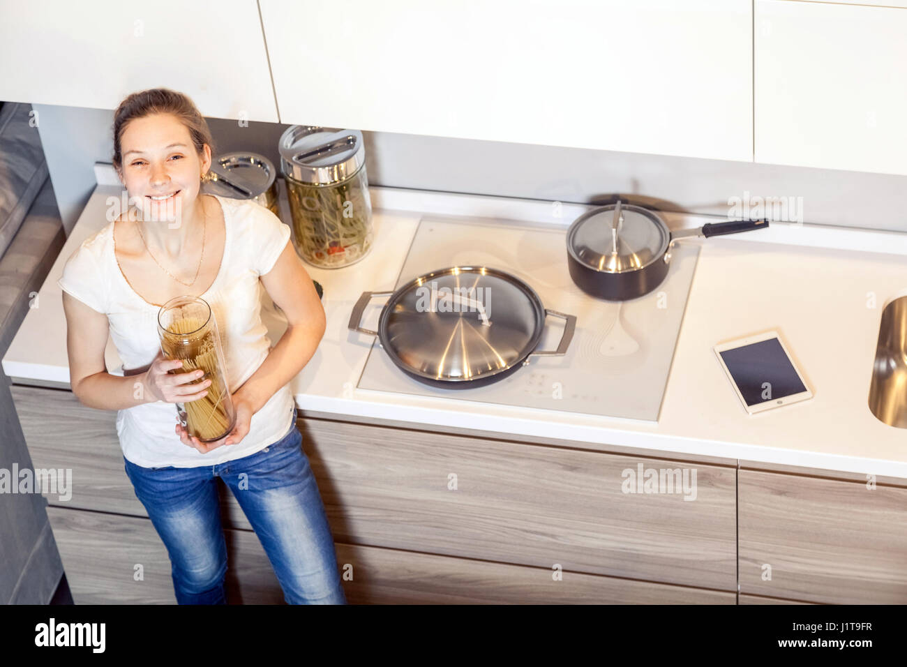 Stets gut gelaunte Frau bereitet Spaghetti Nudeln in der Küche zu Hause, Ansicht von oben. Blick in die Kamera. Stockfoto