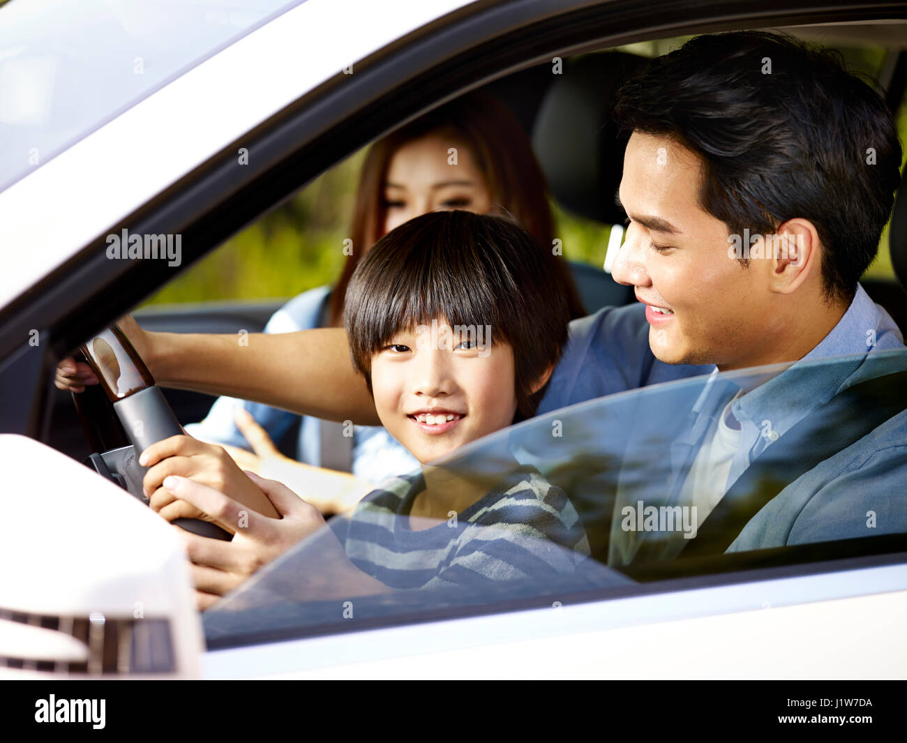 asiatischen Vater seinem Sohn das Lenkrad seines Autos halten lassen. Stockfoto