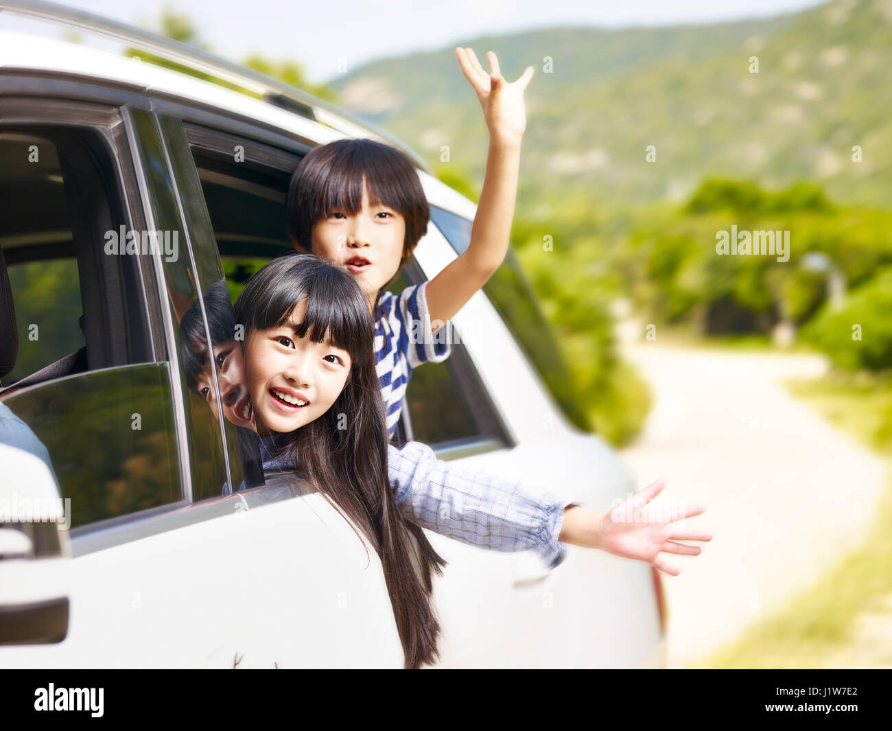 glückliche asiatische Kinder stecken ihre Köpfe aus dem hinteren Fenster während der Fahrt in einem Auto. Stockfoto