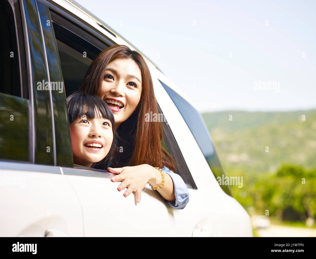 junge asiatische Mutter und Tochter während der Fahrt in einem Auto Heckscheibe ihre Köpfe herausragen. Stockfoto