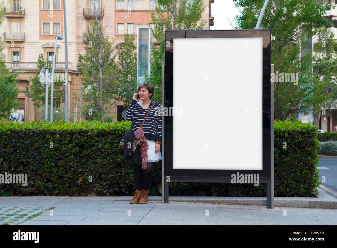 Frau im Gespräch mit Handy, stehend in einer leeren Plakatwand Stockfoto