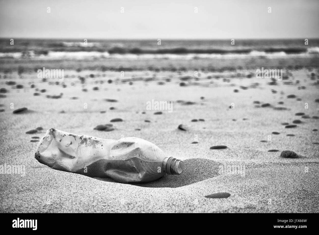 Schwarz / weiß Bild eine Leere Plastikflasche, die auf einen Strand, Tiefenschärfe, Umweltverschmutzung Konzept Bild hinterlassen. Stockfoto