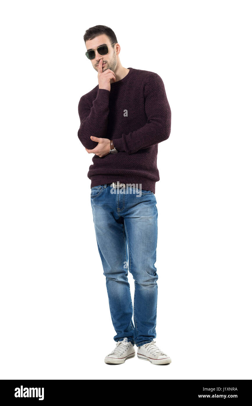 Coole junge zweifelhaft Mann mit Pullover und eine Sonnenbrille, Blick in die Kamera. Ganzkörper-Länge-Porträt über weiße Studio-Hintergrund isoliert. Stockfoto