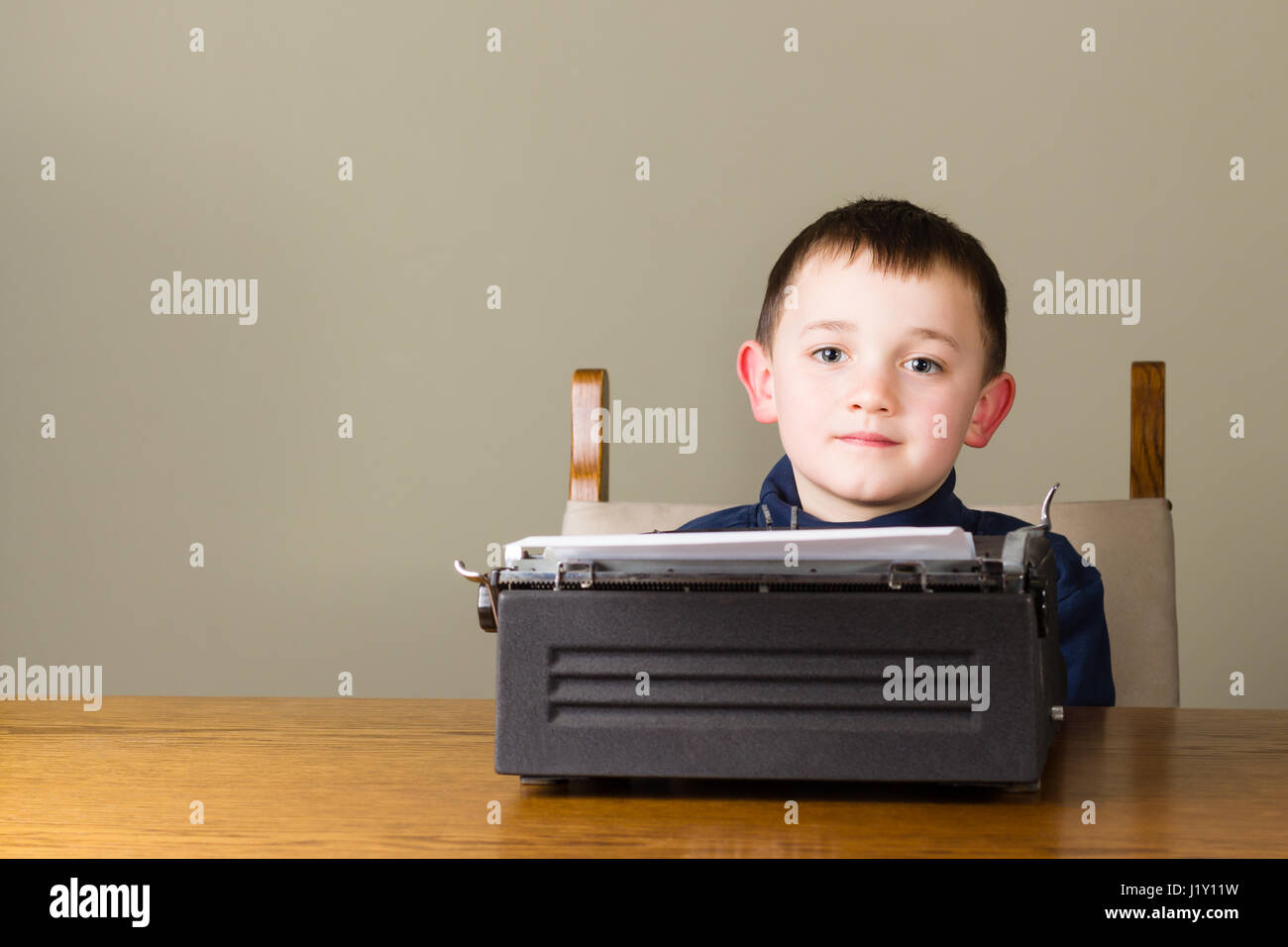 Niedlicher kleine Junge sieht während der Arbeit mit einer alten Vintage schwarze Schreibmaschine zu Hause abgelenkt Stockfoto