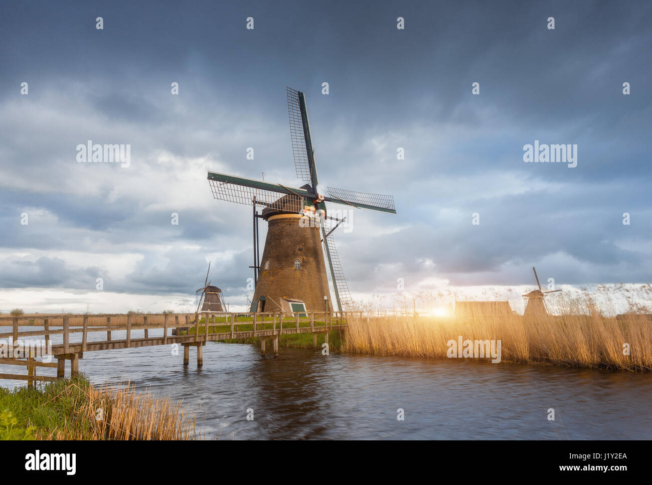 Erstaunliche Windmühlen bei Sonnenuntergang. Rustikale Landschaft mit traditionellen holländischen Windmühlen, Brücke in der Nähe der Wasserkanäle und blauen Wolkenhimmel. Abends bedeckt Stockfoto